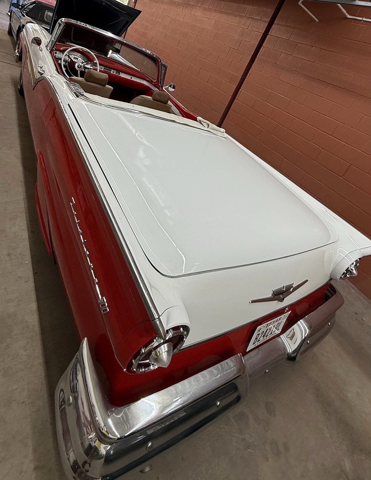Red-and-white Ford Fairlane convertible from behind, white tonneau deck, chrome bumper and round tail lights